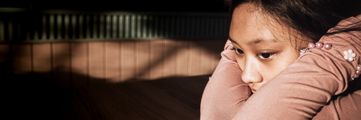 Ein Mädchen liegt mit dem Kopf auf den verschränkten Armen auf einem Tisch und wirkt nachdenklich oder traurig.